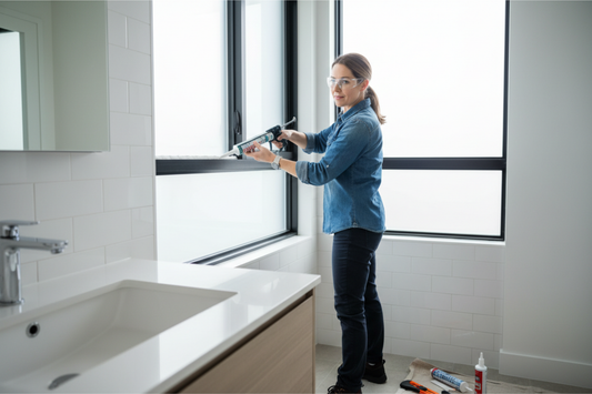 Woman using caulking gun to seal bathroom window in Mississauga home with proper technique